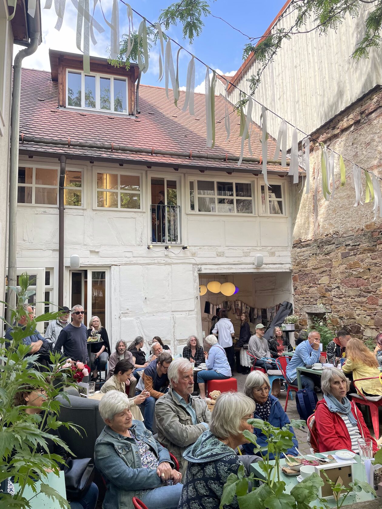 Innenhof der alte Sellerie, in der die Kulturküche beheimatet ist. Im Hof sitzen viele Menschen und unterhalten sich. Im Hof ist eine Girlande gespannt.