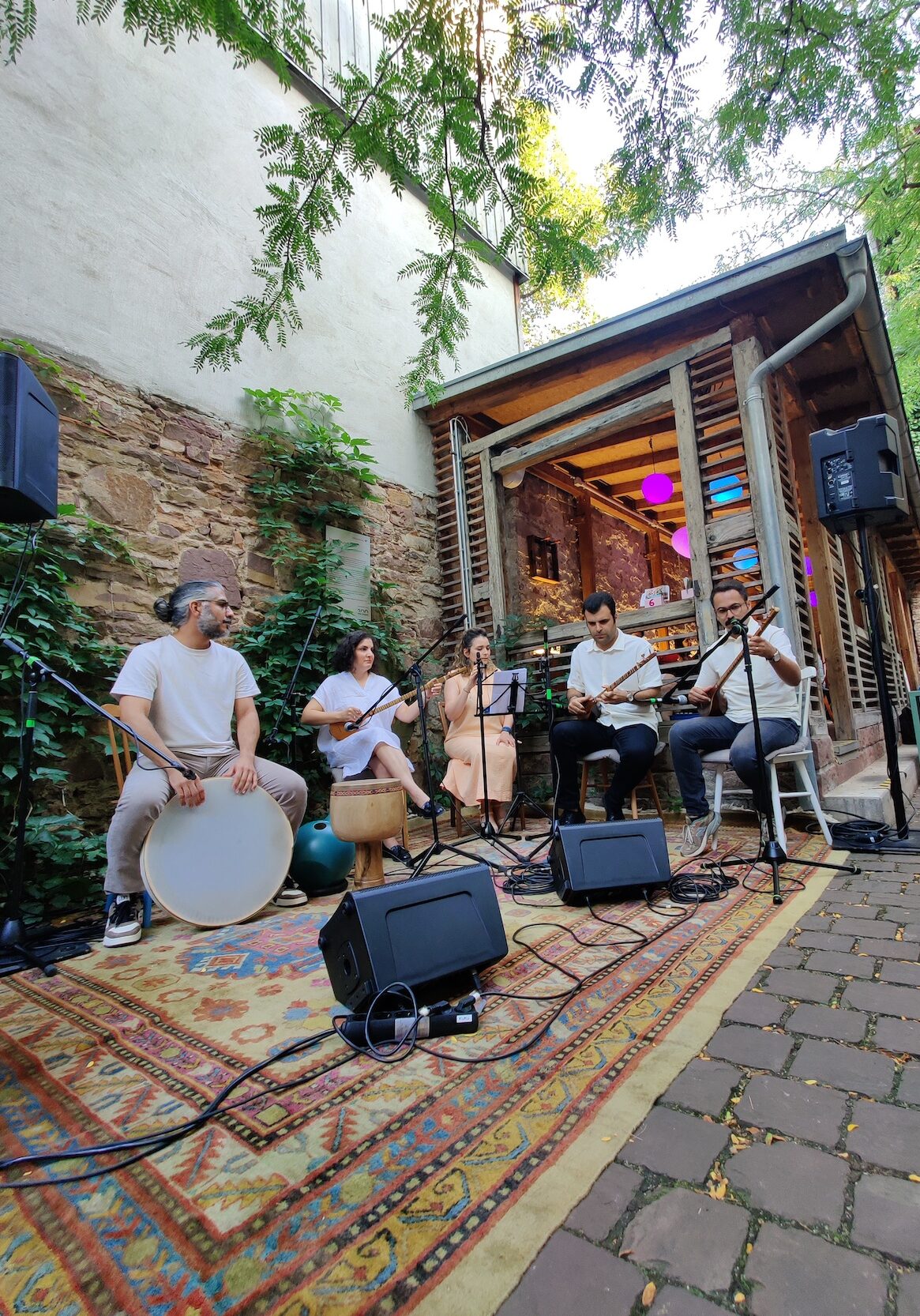 Im Innenhof ist ein Teppich ausgerollt. Auf ihm ist eine kleine Bühne aufgebaut. Es spielen fünf Personen Musik.