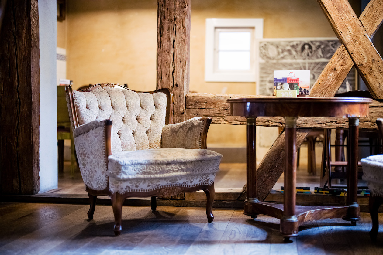 Raum der Kulturküche mit alten Holzbalken und gemütlichem Sessel. Neben dem Sessel steht ein alter Holztisch.