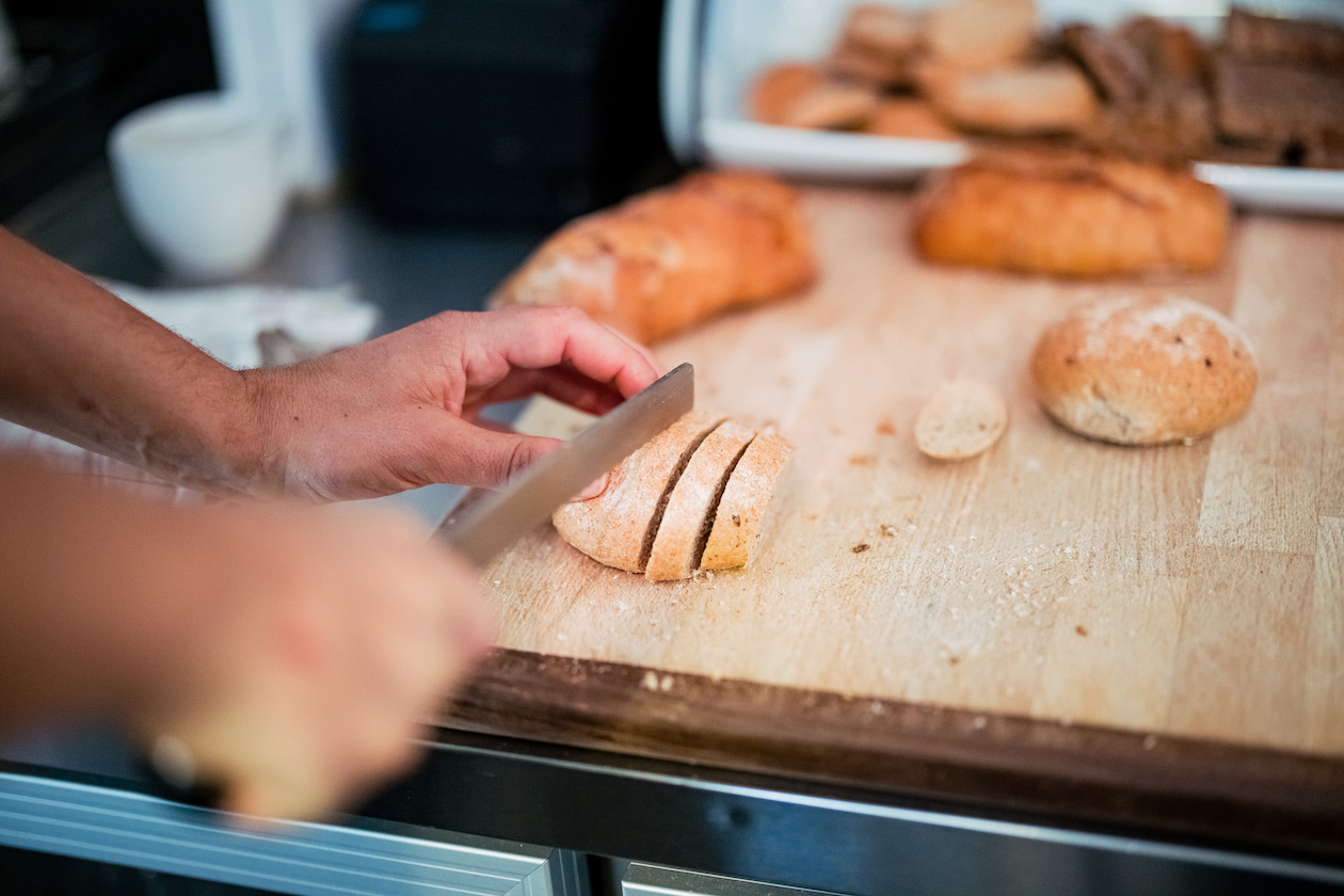Holzbrett, auf dem eine Person mit einem großen Messer Brot schneidet.