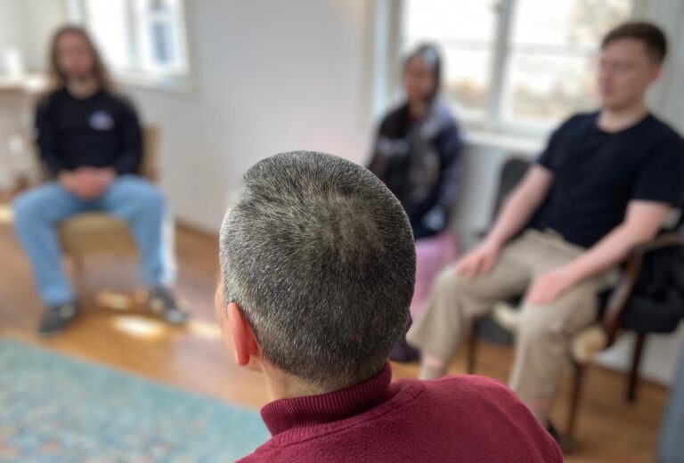 Vier Personen sitzen in einem Raum auf Stühlen mit geschlossenen Augen