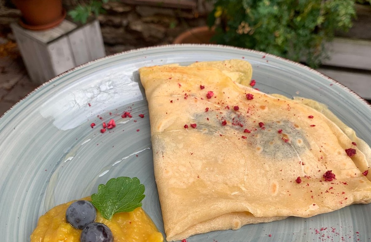Teller mit einem Crêpe, daneben ein Fruchtmus und Heidelbeeren.