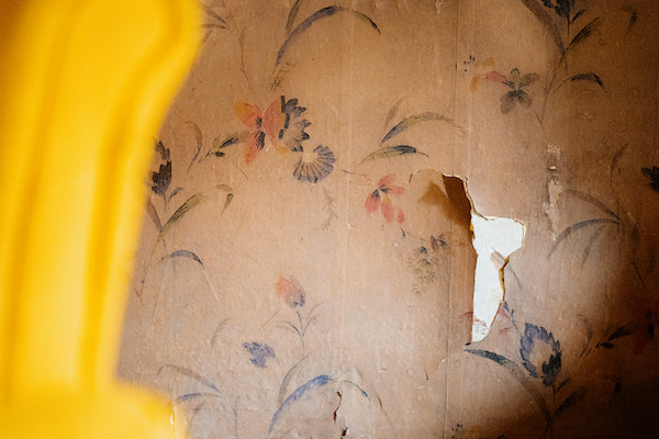 Tapete mit Blumenmuster, ein Teil der Tapete löst sich.