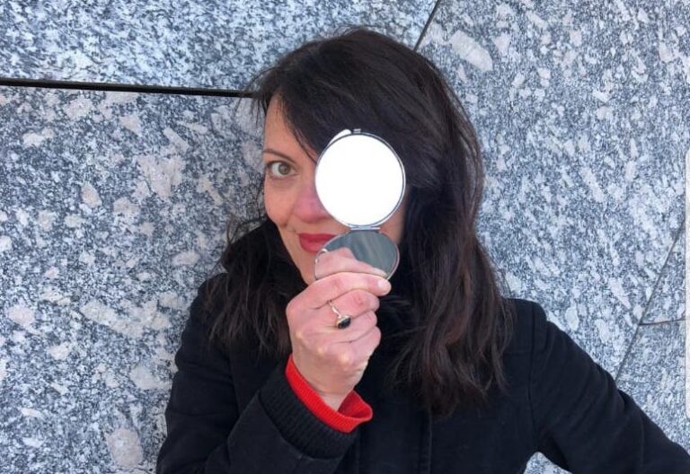 Iba, die Leiterin des Workshops, schaut in die Kamera und hält vor das eine Auge einen Spiegel.