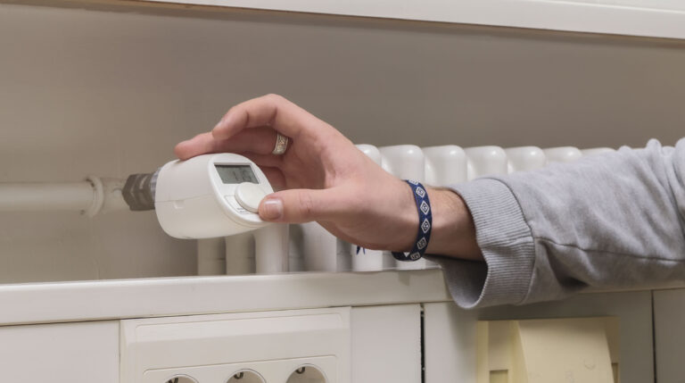 Hand dreht an einem Heiz-Thermostat.
